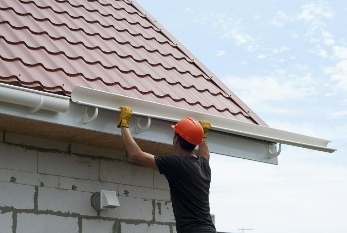 Worker lifting a new gutter run into place along a roofline